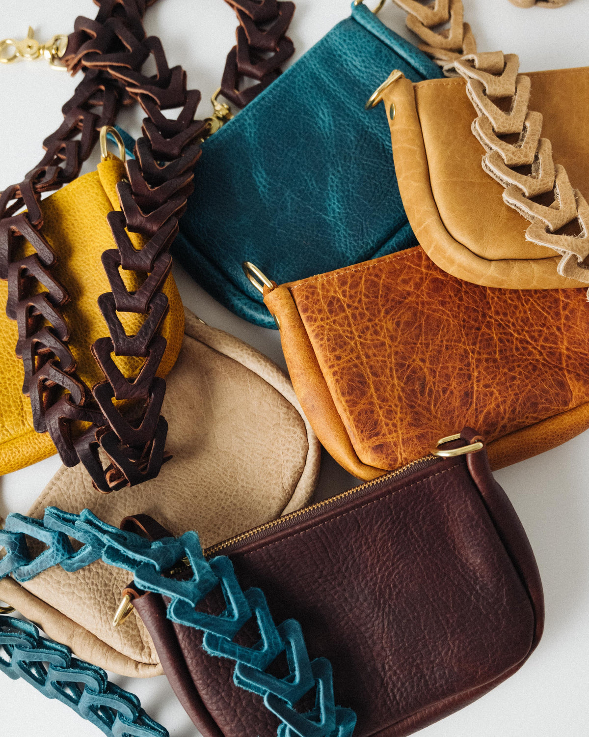 Handmade full-grain leather mini crossbody bags in various colors with solid brass zippers and unique braided straps.