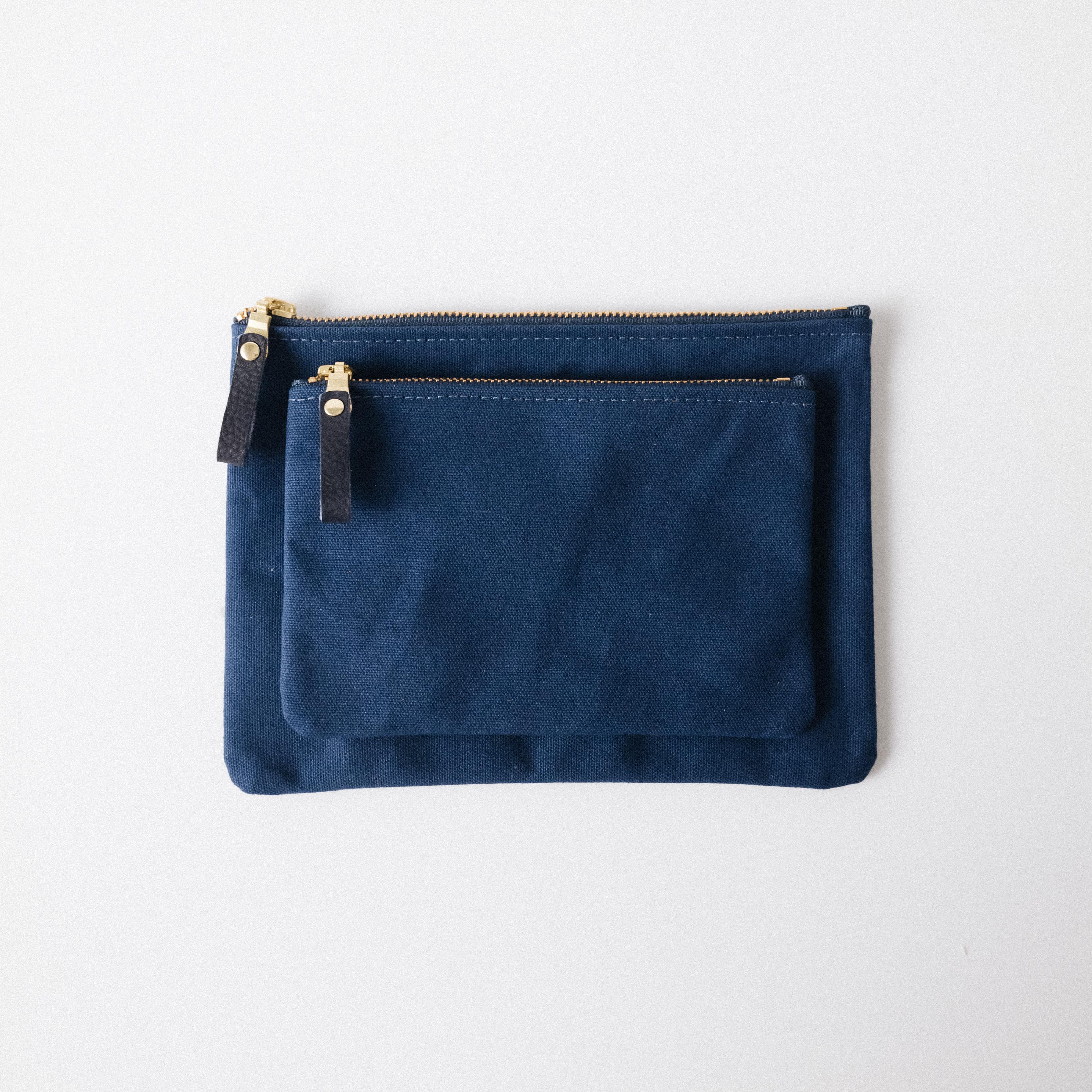 Two navy blue heavyweight cotton canvas zip pouches with solid brass zippers and leather pulls.