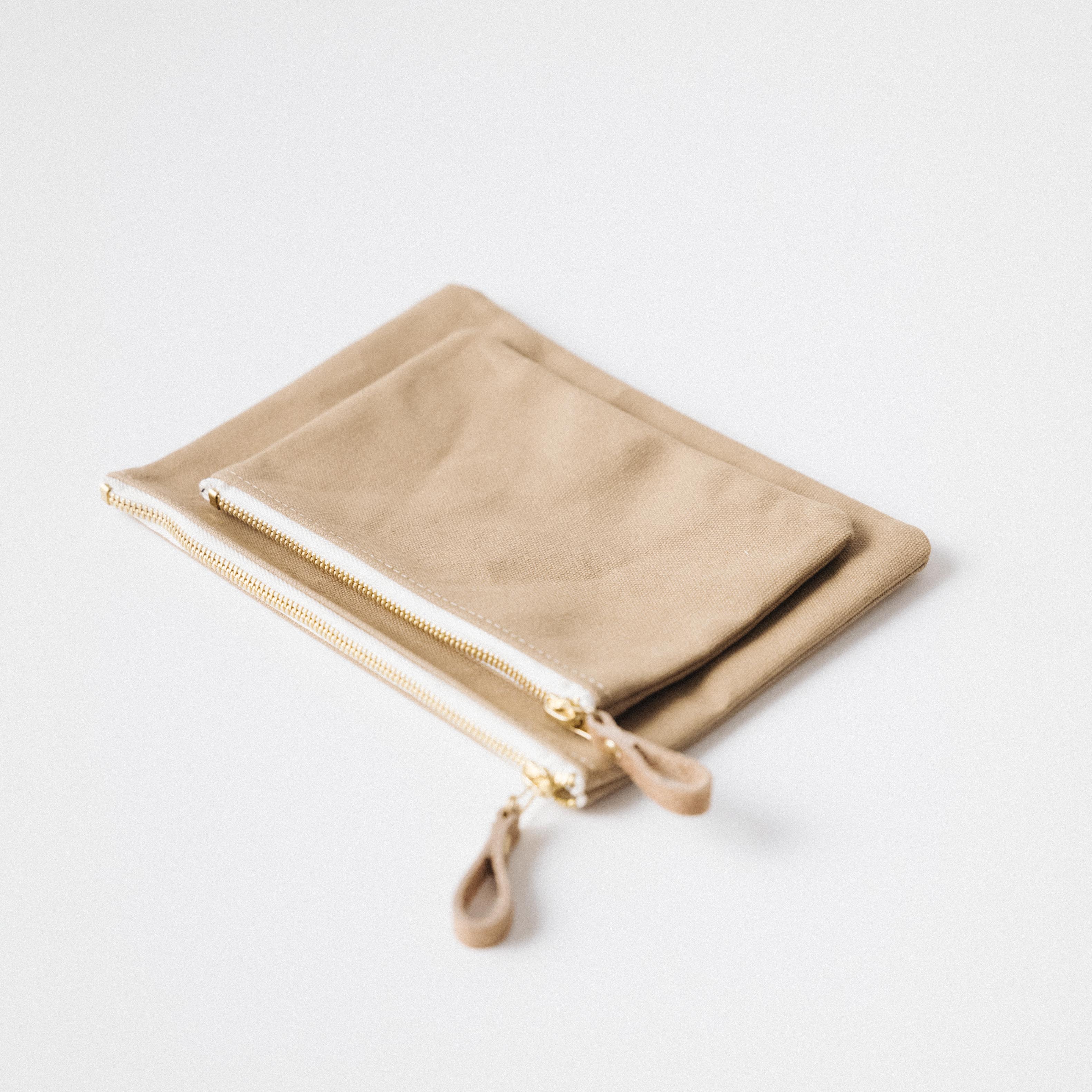 Two tan heavyweight cotton canvas zip pouches with solid brass zippers and leather pulls.