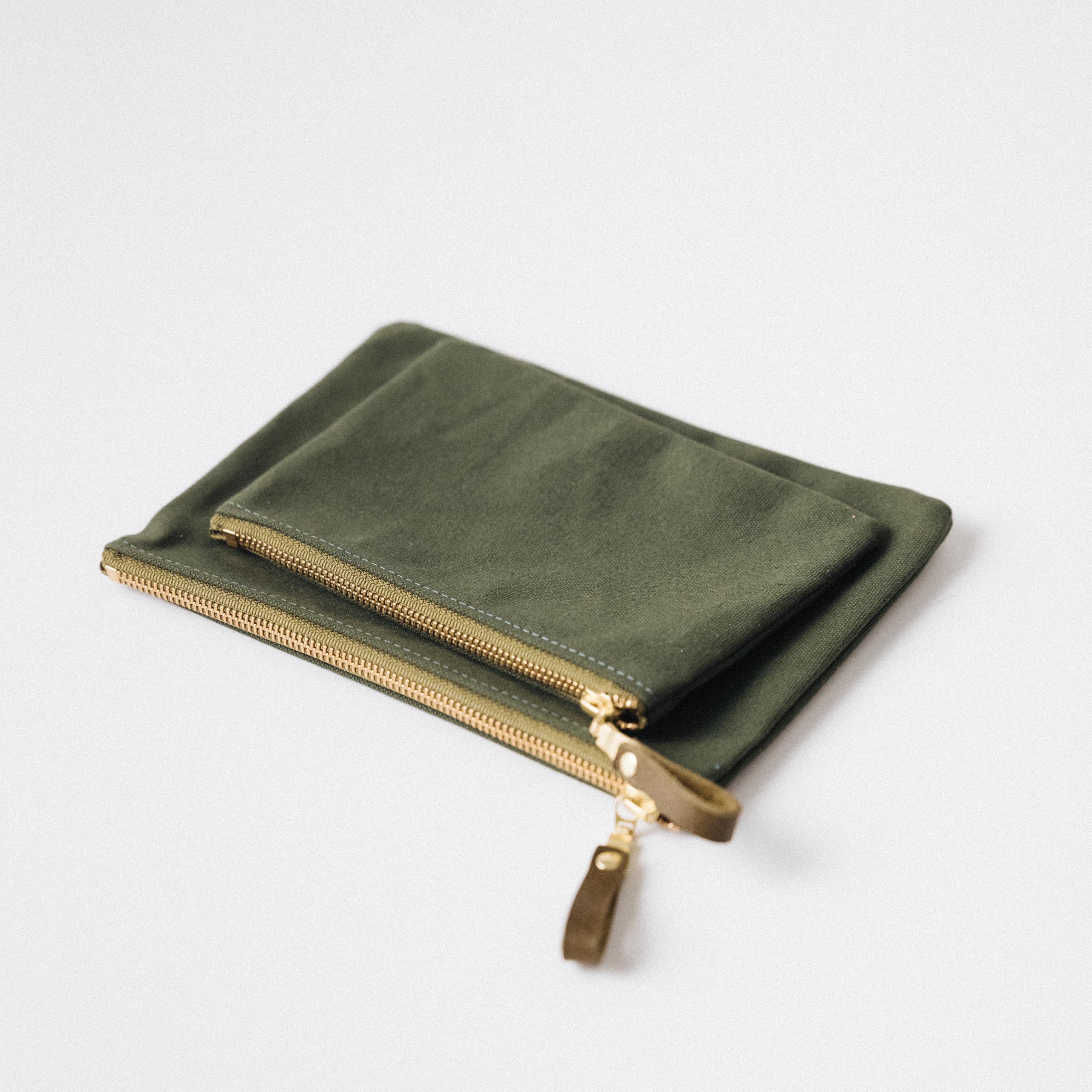 Olive green heavyweight cotton canvas zip pouches with solid brass zippers and leather pulls in small and medium sizes.