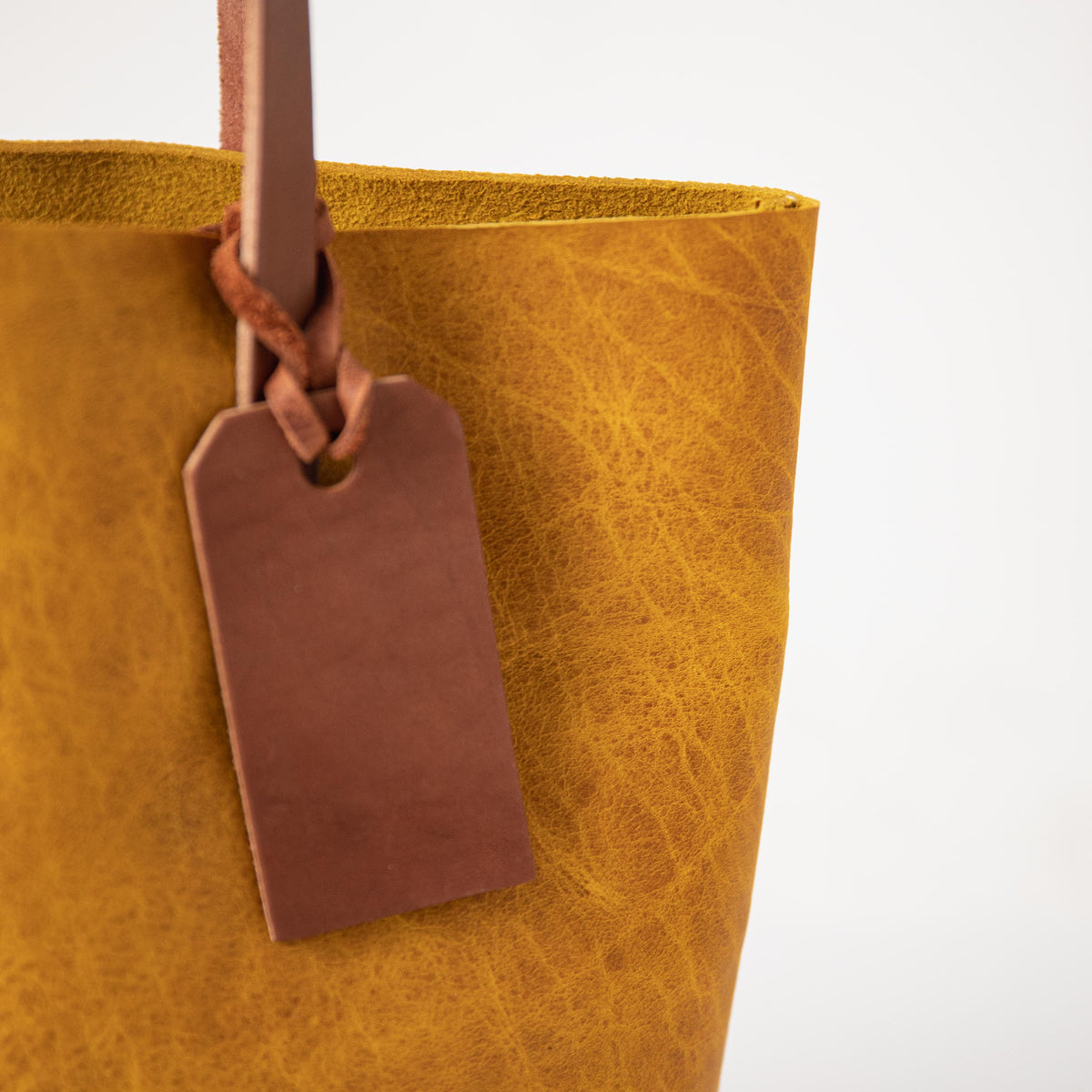 Yellow Bison Tote: close-up of vibrant yellow leather with prominent grain, tan handle, and free customizable tag.