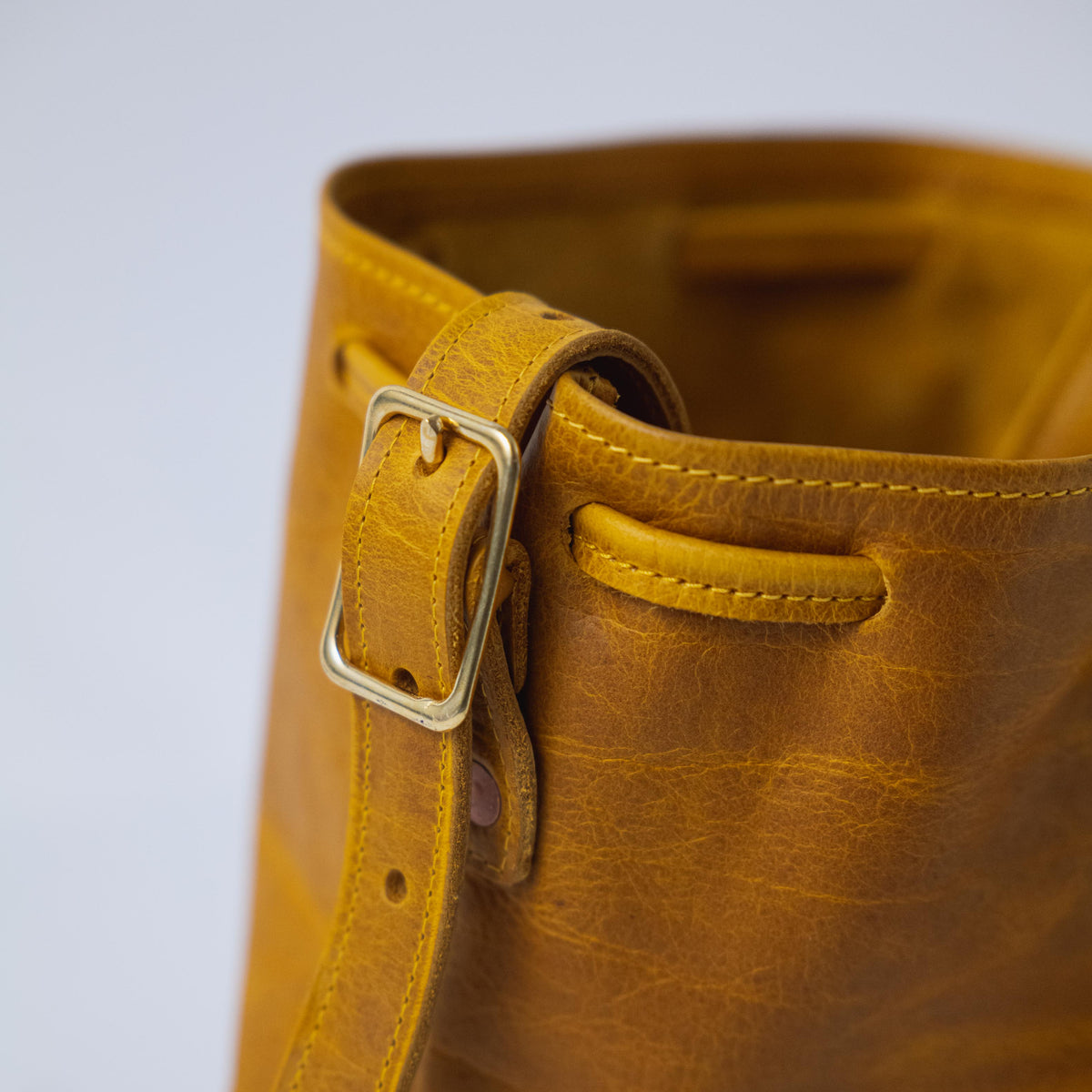 Close-up of the Yellow Bison Bucket Bag, showcasing its vibrant full-grain leather, brass buckle, and drawstring closure.